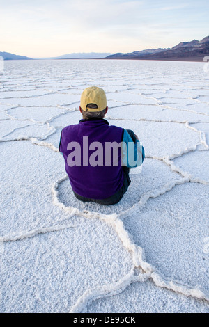 Ein Mann sitzt in geometrischen Mustern Salzpfanne in der Nähe von Badwater im Death Valley Nationalpark, Kalifornien. Stockfoto