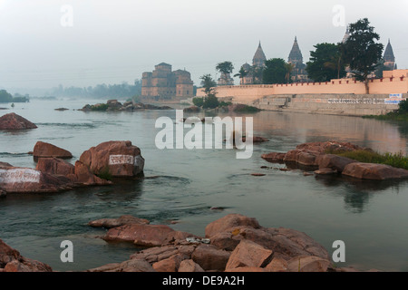 Ghat und Bundela Cenotaphs erscheinen in den frühen Morgenstunden über nebligen Betwa Fluß, Indien Orchha. Stockfoto