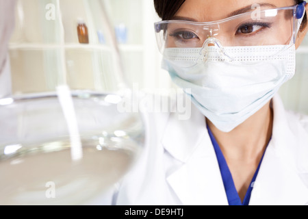 Chinesische asiatische medizinische oder wissenschaftliche Forscherin oder Arzt mit Blick auf eine konische Flasche klare Flüssigkeit im Labor Stockfoto