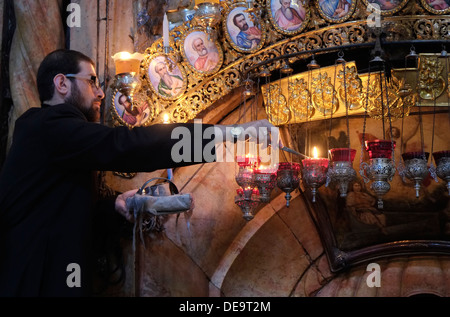 Ein griechisch-orthodoxer Geistlicher zündet am Eingang der Rotunde Edicule oder Anastasia an, die die Engelskapelle enthält, eine Vorkammer, die zum Grab Jesu Christi führt, in der Kirche des Heiligen Grabes in der Altstadt von Jerusalem, Israel. Stockfoto