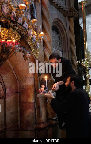 Ein griechisch-orthodoxer Geistlicher zündet am Eingang der Rotunde Edicule oder Anastasia an, die die Engelskapelle enthält, eine Vorkammer, die zum Grab Jesu Christi führt, in der Kirche des Heiligen Grabes in der Altstadt von Jerusalem, Israel. Stockfoto