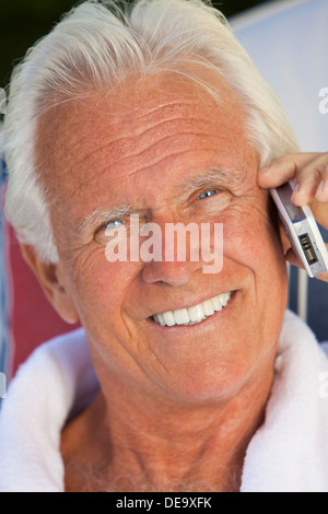 Porträt von attraktiven hübschen senior glücklich in einem weißen Bademantel sitzen außen Lächeln auf den Lippen reden auf seinem Handy Stockfoto