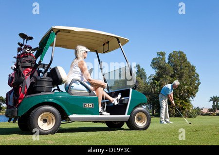 Glücklich senior Mann und paar zusammen Golf spielen, einen Schuss die Frau der Mann trifft Frau sitzt in einem Golfwagen Stockfoto