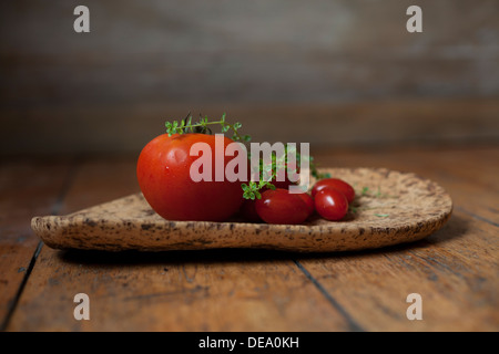 Eine Auswahl von frischen Tomaten und einem Zweig Thymian auf einer Pinnwand. Stockfoto