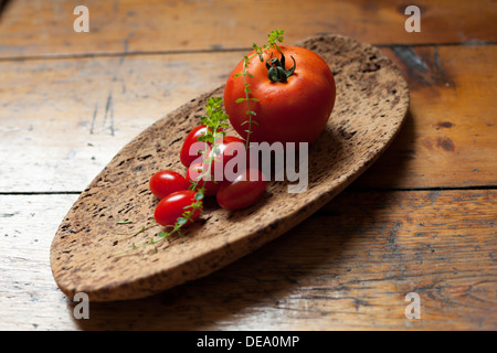 Eine Auswahl von frischen Tomaten und einem Zweig Thymian auf einer Pinnwand. Stockfoto
