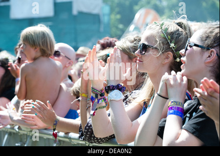 Glückliche hübsche weiße Teenager-Mädchen mit Blumen in den Haaren, Armreifen an ihren Handgelenken an der Vorderseite einer Barriere auf einem Sommer-Musikfestival Pre-Covid Stockfoto