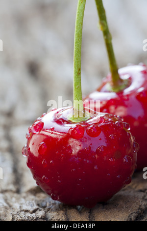 Extreme Nahaufnahme von einer frische Kirschen mit Stiel und großen glitzernden Wassertropfen auf einem alten Holztisch Stockfoto