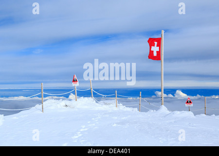 Ein Foto von einer Schweizer Flagge in der Jungfrau-Region der Schweiz. Die Gipfel sind über den Wolken und es regnet weiter unten. Stockfoto