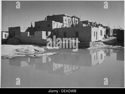 Seitenansicht eines lehmhauses in Acoma Pueblo, einem National Historic Landmark in New Mexico, mit Wasser im Vordergrund. Das Haus aus lehmziegel spiegelt die traditionellen Bautechniken der indianischen Architektur wider, wobei das Pueblo eine bedeutende kulturelle Stätte ist. Stockfoto