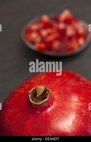 Nahaufnahme eines saftigen reifen Granatapfels, verschwommen im Hintergrund einen Löffel mit Granatapfel Samen Stockfoto