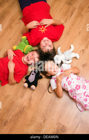 Mädchen, 4 Jahre, und jungen, 6 und 11 Jahren, auf dem Boden liegend, lachen, mit Plüsch-Spielwaren Stockfoto