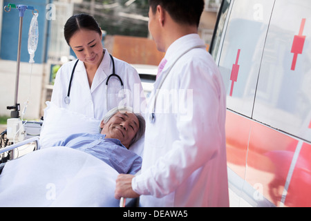 Zwei Ärzte, die Machenschaften bei einem älteren Patienten auf einer Bahre vor einen Krankenwagen Stockfoto