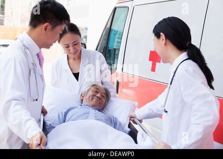 Drei Ärzte Machenschaften bei einem älteren Patienten auf einer Bahre vor einen Krankenwagen Stockfoto