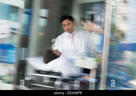 Zwei Ärzte, die bei einem Patienten auf einer Bahre durch die Türen des Krankenhauses Machenschaften Stockfoto