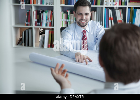 Zwei lächelnde Architekten diskutieren über eine Blaupause im Büro, Stockfoto