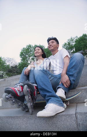 Junge Brautpaar sitzen und ruhen auf konkrete Schritte außerhalb mit einem Skateboard und Roller-blades Stockfoto