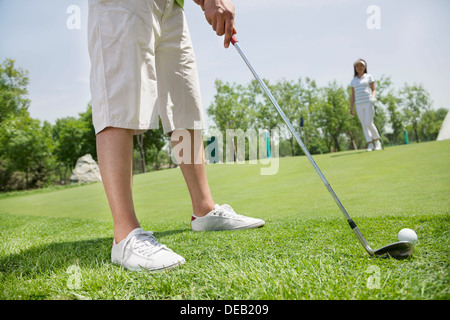 Geringer Teil der junge Mann den Ball auf dem Golfplatz, Frau im Hintergrund Stockfoto