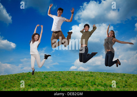 Vier lächelnden Freunde springen in der Luft, Himmel und Wolken Hintergrund Stockfoto