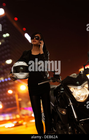 Junge Frau mit Sonnenbrille am Telefon sprechen und stand neben ihrem Motorrad in der Nacht in Peking Stockfoto
