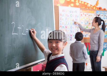 Schulmädchen tun mathematische Gleichung am schwarzen Brett Stockfoto