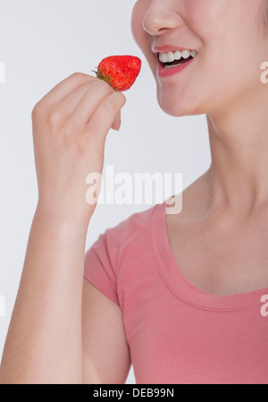 Junge Frau in rosa Hemd Essen eine Erdbeere, Studio gedreht, halbe Gesicht zeigen Stockfoto