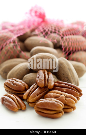 Geschälte Pekannüsse vor einem saldierten Beutel ungeschälte Pekannüsse auf weißem Hintergrund. Stockfoto