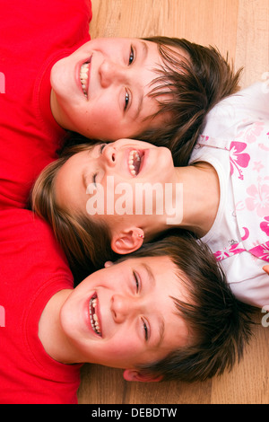 Mädchen, 4 Jahre, und jungen, 6 und 11 Jahren, auf dem Boden liegend, lachen Stockfoto