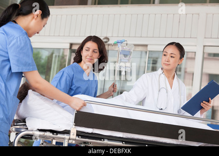 Weibliche Sanitäter und Arzt bei einem Patienten auf einer Bahre vor dem Krankenhaus Machenschaften Stockfoto