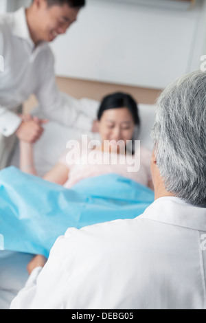 Frauen in den Wehen hielt ihre Ehemänner Hand mit Arzt im Vordergrund im Krankenhaus Stockfoto