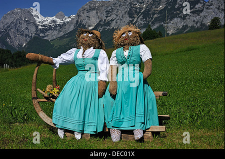 Zwei Stroh Puppen oder Figuren im Dirndl Kleider sitzen auf einem Schlitten mit lange Horn-förmigen Läufer auf einer Wiese Stockfoto