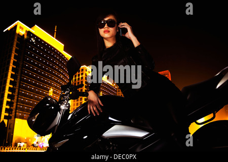 Schöne junge Frau mit Sonnenbrille am Telefon sprechen und stützte sich auf ihrem Motorrad in der Nacht Stockfoto