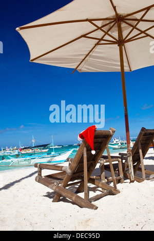 Sonnenschirm mit Santa Claus Hut auf Stühlen Stockfoto