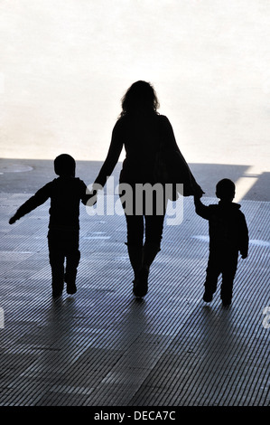 Eine Frau mit zwei Kindern in der Hand geht out of the Dark und ins Licht Stockfoto
