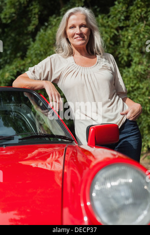 Lächelnde Reife Frau lehnte sich gegen ihre roten cabriolet Stockfoto