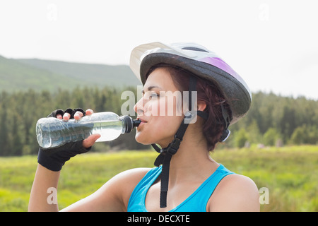 Sportliche Frau mit Fahrrad Helm Trinkwasser Stockfoto