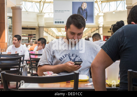 Ein junger Mann Mitte 20, in sein Handy vertieft ist, beim Essen in einem Food Court in einem Einkaufszentrum. Oklahoma City, Oklahoma, USA. Stockfoto