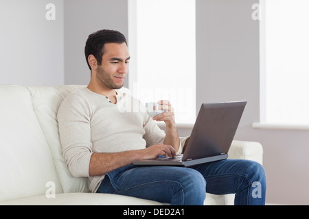 Entspannte attraktiver Mann halten Kaffee während der Arbeit an seinem laptop Stockfoto