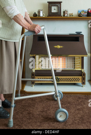 Ältere Dame in ihre neunziger Jahre mit zu Fuß Rahmen in der Nähe Gas Feuer. Stockfoto