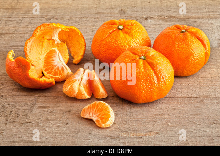 Mandarin-Orangen - Mandarinen auf einer rustikalen Holzoberfläche, drei ganz, geschält und segmentiert. Stockfoto