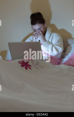 Hübsche Teen trägt Bademantel beobachten ihren Laptop im Dunkeln Stockfoto