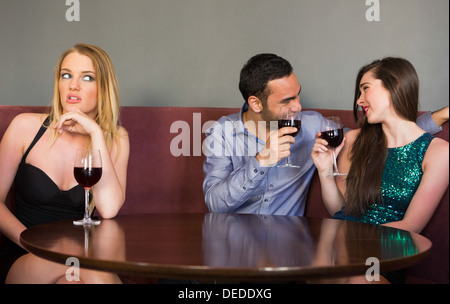 Blonde Frau, einsam, wie zwei Personen neben ihr flirten sind Stockfoto