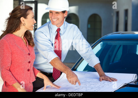 Mann im harten Hut, Hemd und Krawatte auf Baustelle mit Frau, Architekt Blau gedruckten Pläne betrachten. Stockfoto