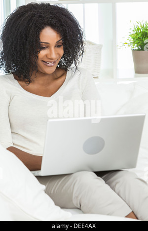 Schönen lächelnden afroamerikanische Frau zu Hause sitzen auf Sofa oder Couch mit ihrem Laptop-Computer. Stockfoto