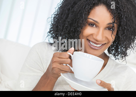 Schönes Lächeln auf den Lippen afroamerikanische Frau zu Hause sitzen auf Sofa oder Sofa Tasse Kaffee oder Tee trinken Stockfoto