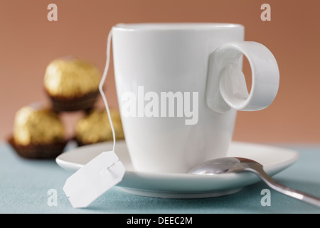 Nahaufnahme eines weißen Tasse und Untertasse mit Pralinen im Hintergrund Stockfoto