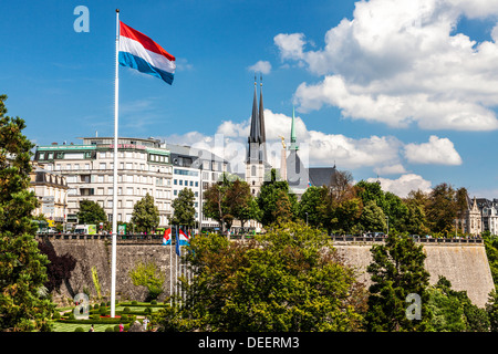 Blick auf den Petrusse Valley Park, das Grand Hotel Cravat und Kathedrale Notre-Dame. Luxemburg-Flagge weht vor blauem Himmel. Stockfoto