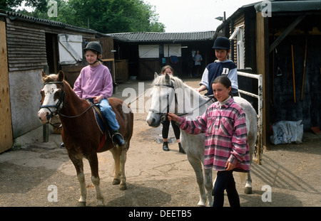 Kinder auf ihren Ponys reiten lernen aus dem Stall geführt Stockfoto