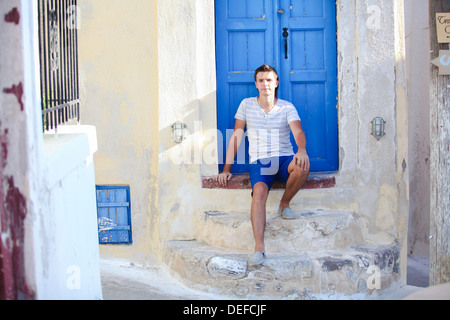 Junger Mann sitzt in der Nähe von alte blaue Tür von Emporio Dorf auf der Insel Santorini, Griechenland Stockfoto