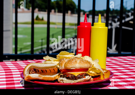 Heckklappe Partei mit Cheeseburger, Hot Dog, Pommes Frites und Senf und Ketchup-Flaschen. Fußballplatz im Hintergrund. Stockfoto