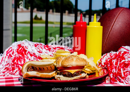 Nachlaufen Partei mit Cheeseburger, Hot Dog, Pommes frites, Pompons und Fußball. Fußballplatz im Hintergrund. Stockfoto